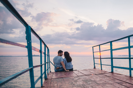 lovely couple sitting on the pier and looking on sunriseの写真素材
