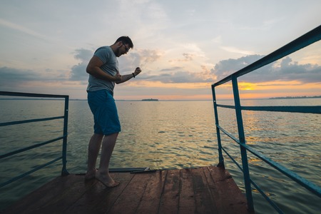 man rises hands up on the lake pier on sunriseの写真素材