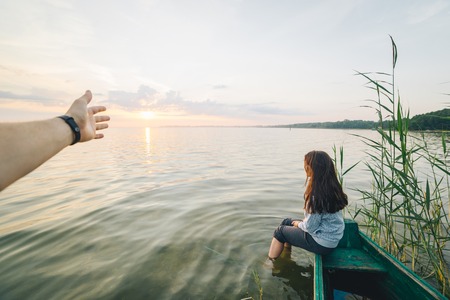 first person view , man looking on girl that sitting on old boat and looking on sunriseの写真素材