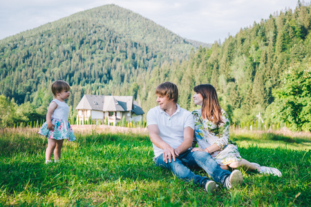 parents play with daughter on the field with mountains on backgroundの写真素材