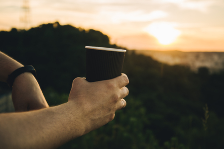 man hands hold cup of coffee with beautiful view of sunset on backgroundの写真素材