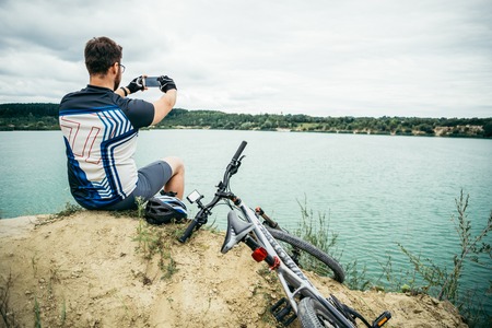 man sitting on the peak of the hill with bicyle and taking picture of the viewの写真素材