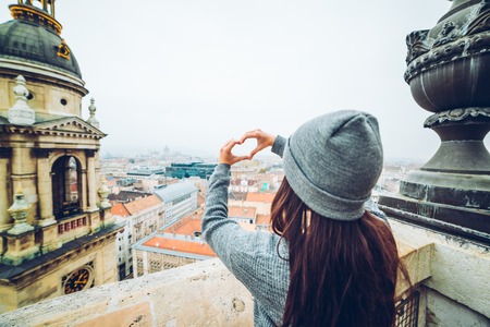 woman shows heart with hands with beautiful view of old european city on backgroundの写真素材