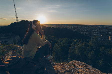 young pretty woman listing music on the top of the hill on sunsetの写真素材