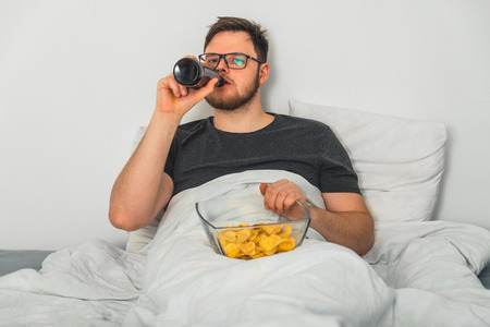 man in bed with beer and snacksの写真素材