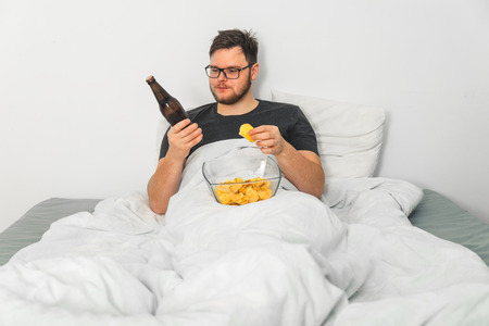 man in bed with beer and snacks watching TVの写真素材