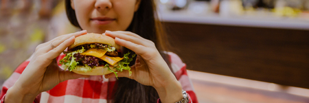 young woman eat cheeseburger hold in hand in fron of faceの写真素材