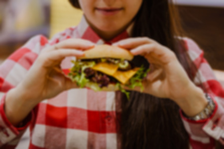 young woman eat cheeseburger hold in hand in fron of faceの写真素材