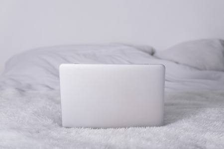 white laptop on white bed with white fluffy blanketの写真素材