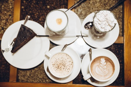 view from above four cup of warm up drink on the table with piece of cakeの写真素材