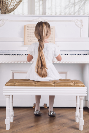 little blond girl play on white piano in white dressの写真素材