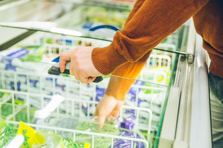 man get frozen food from fridge in store. shopping conceptの写真素材