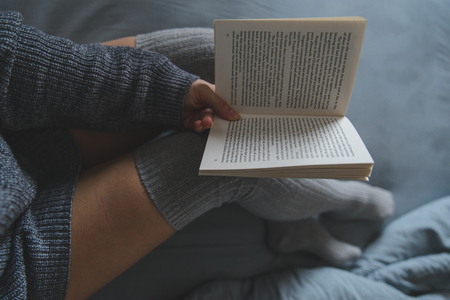 woman read book in bed with grey sheetsの写真素材