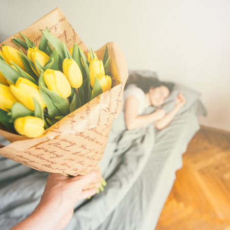 first person view. man bring flowers to bed for sleeping girlfriend. romantic surprise conceptの写真素材