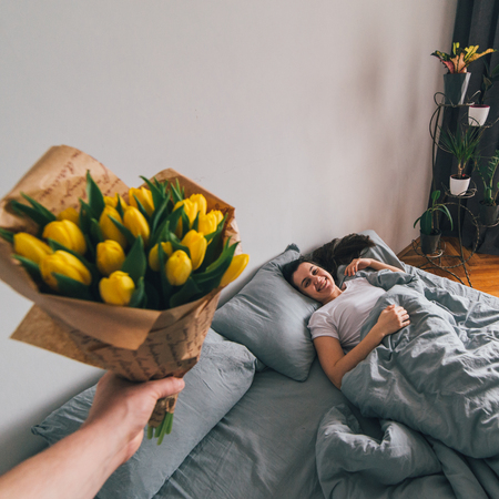 first person view. man bring flowers to bed for sleeping girlfriend. romantic surprise conceptの写真素材