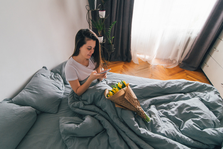 woman take picture of bouquet of yellow tulips. romantic surprise in bedの写真素材