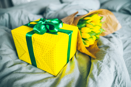 bouquet of yellow tulips with yellow gift box on bed with grey sheets. morning sun light shine through windowの写真素材