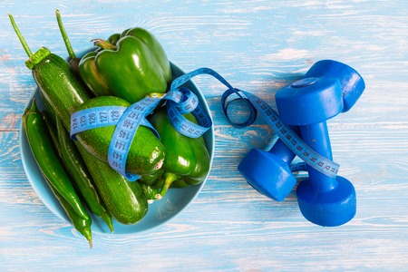 dumbbells with green fresh fruits and vegetables on plate on blue wooden backgroundの写真素材