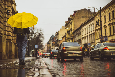 woman walk by side walk with yellow umbrella. rainy weather in old european cityの写真素材