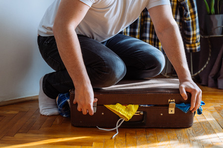 man need help to close suitcase. overloaded bag with clothes. travel conceptの写真素材