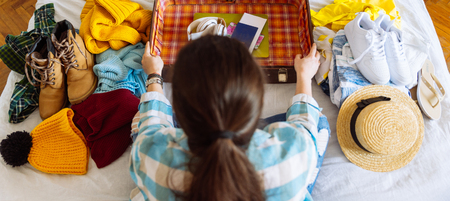 woman sit on bed with suitcase and clothes around. travel concept. decide warm or cold country to go.の写真素材