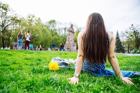 woman sitting on grass in city park with yellow flowers. view from behindの写真素材