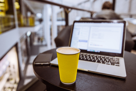 yellow coffee cup on table. laptop with cellphone on background. freelancer conceptの写真素材