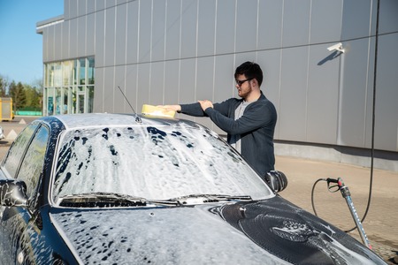 young man in sunglasses washing car at self service carwashの写真素材
