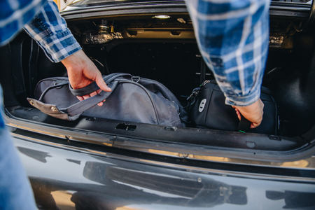 young adult man putting bag in car trunk. car travel conceptの写真素材