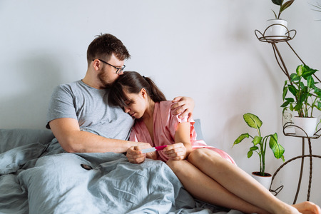 sad couple in bed looking at negative pregnancy testの写真素材