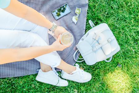 woman holding cup with cool drink while sitting on blanket on grassの写真素材