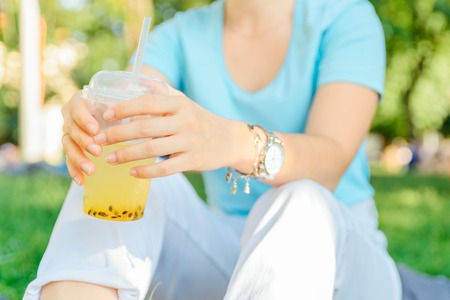 woman holding cool drink in city park. blurred background. wide angel