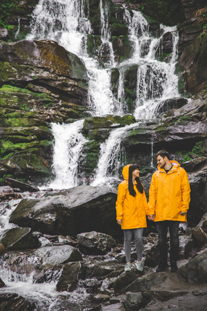 couple standing in yellow raincoat. waterfall on backgroundの写真素材
