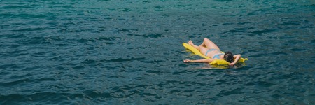young adult woman on yellow mattress in blue sea water. summer time concept.