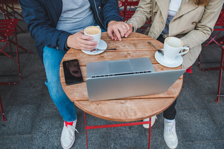 couple holding hands while drinking latte in outdoors cafe. close up