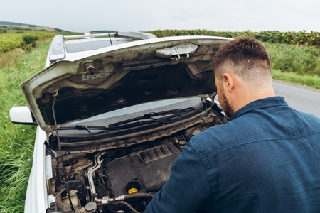 man looking at engine at broken car at roadside. road trip problemsの写真素材