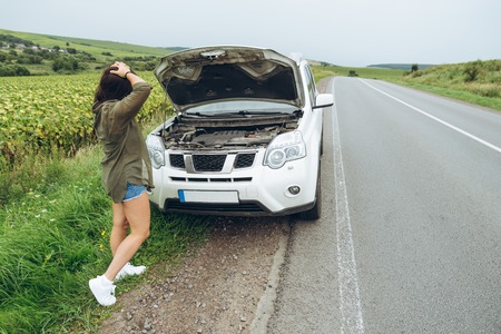 young adult woman standing near broken car on highway and talking on phone. calling car service