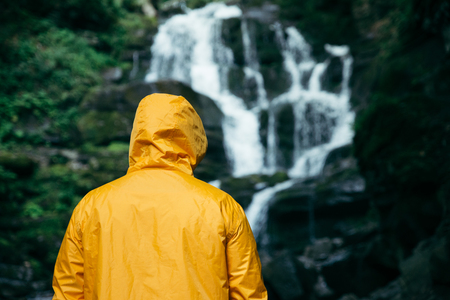 man standing in yellow raincoat and looking at waterfall. hiking conceptの写真素材