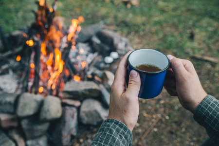 first point of view. man drinking tea in metal cup near camp fire. hikingの写真素材