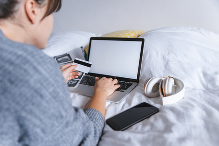 american young adult woman check medical results holding card in hand. laptop with white screen on the bed. copy space. healthcare concept.. health insuranceの写真素材
