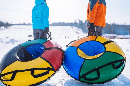 two persons pull sleighs to the top of the hill. snow tubing. winter activityの写真素材