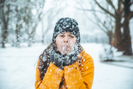 woman blowing snow from her hands. snowed park on background. winter season concept