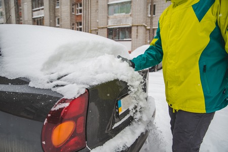 man cleaning his car after snow storm. winter time