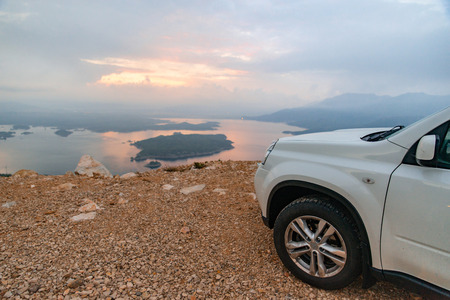white suv car at cliff sunrise over lake on background. road tripの写真素材