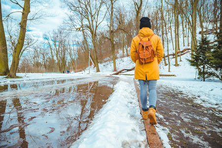 woman walking by city park passing puddles around. melting snow. snow is comingの写真素材