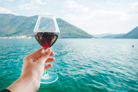 woman hand holding glass of red wine mountains and seaside on backgroundの写真素材