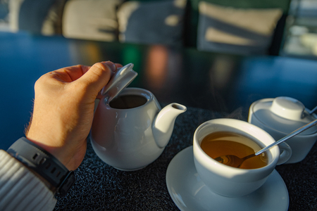 man hand holding cup with tea. kettle on background. sunlightの写真素材
