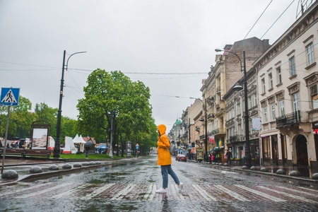 woman in the middle of the street crossing road in yellow raincoat. urban casual clothesの写真素材
