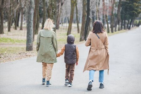 two women walking by city park with little kid. autumn seasonの写真素材