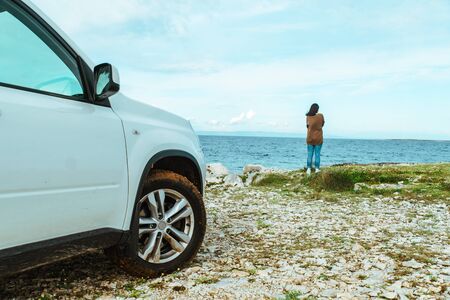 woman standing at edge seaside looking at sea car travel concept. off roadの写真素材